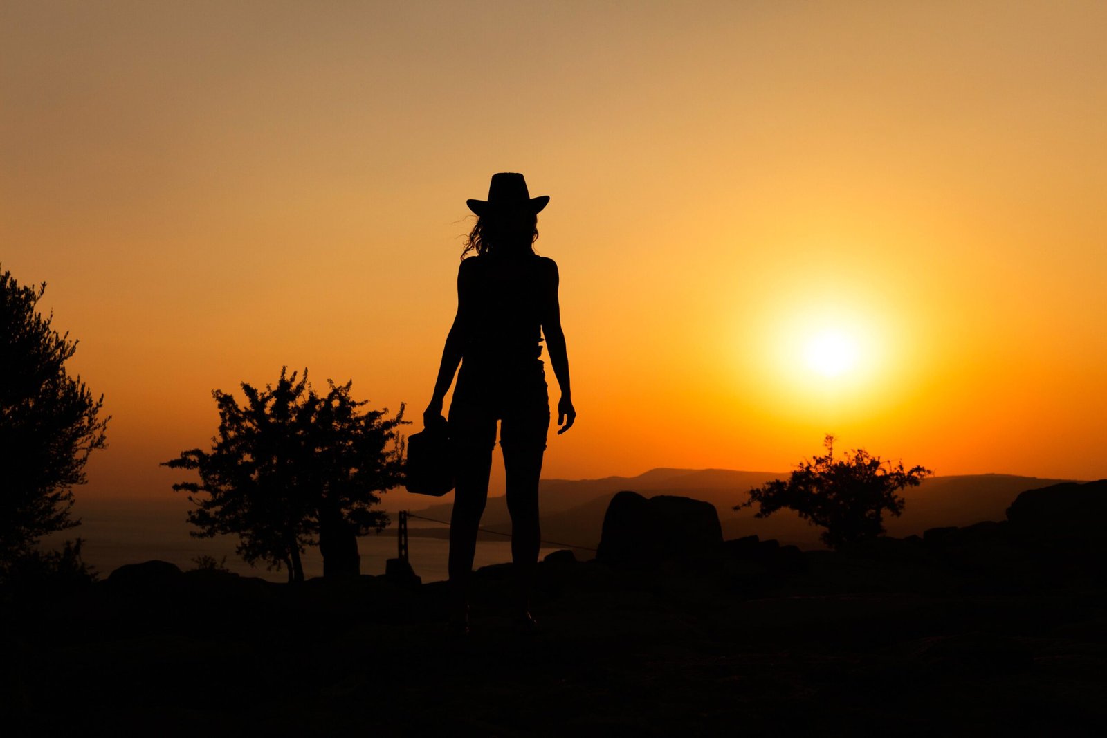 Silhouette of a woman with cowboy hat against a vibrant orange sunset, capturing a tranquil moment.